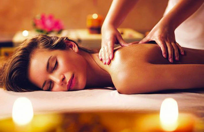 Người phụ nữ thư giãn trong buổi massage với ánh nến dịu nhẹ, không gian spa ấm áp và thoải mái.