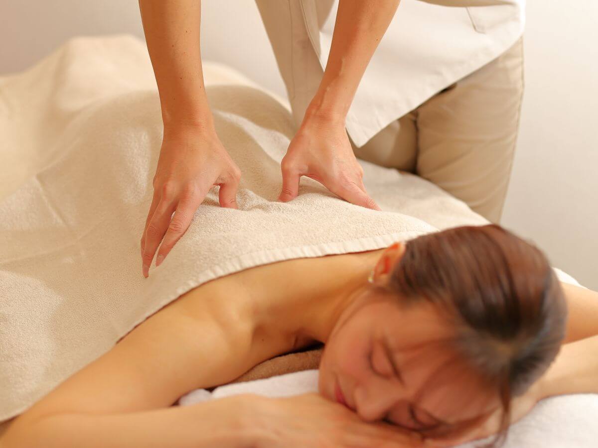 Người phụ nữ thư giãn trong liệu pháp massage toàn thân, tay của liệu pháp viên đang thao tác trên lưng.