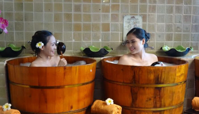 Hai người phụ nữ tắm thư giãn trong thùng gỗ, không gian spa thoải mái và sang trọng.