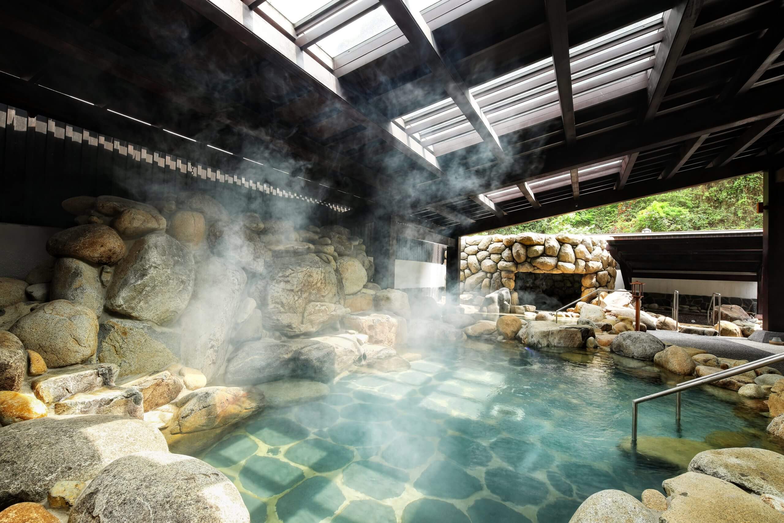 Bể tắm onsen nước nóng với đá tự nhiên và hơi nước tại khu nghỉ dưỡng truyền thống Nhật Bản.