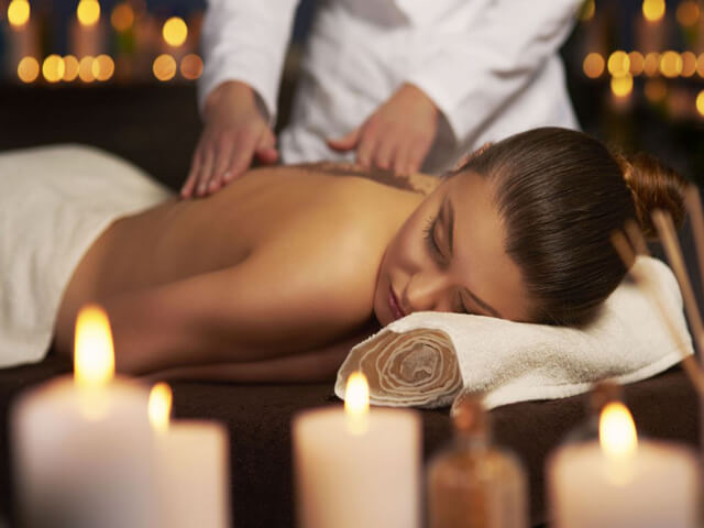 Người phụ nữ thư giãn tại spa với massage giảm stress, nến lung linh tạo không khí ấm cúng và thoải mái.