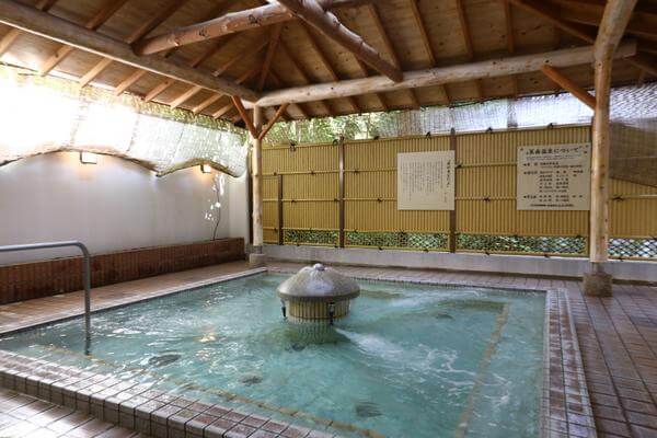 Phòng tắm onsen trong nhà với mái gỗ truyền thống và nguồn nước suối nóng tự nhiên, tạo không gian thư giãn.