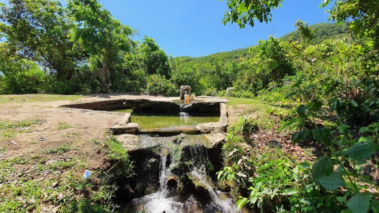 Dòng suối trong lành chảy qua cảnh quan xanh tươi dưới bầu trời xanh, tạo không gian thiên nhiên yên bình.