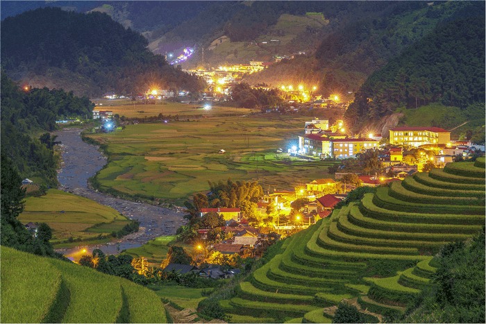 Thị trấn bên ruộng bậc thang về đêm, ánh đèn lung linh, núi rừng bao quanh, cảnh đẹp thanh bình và thơ mộng.