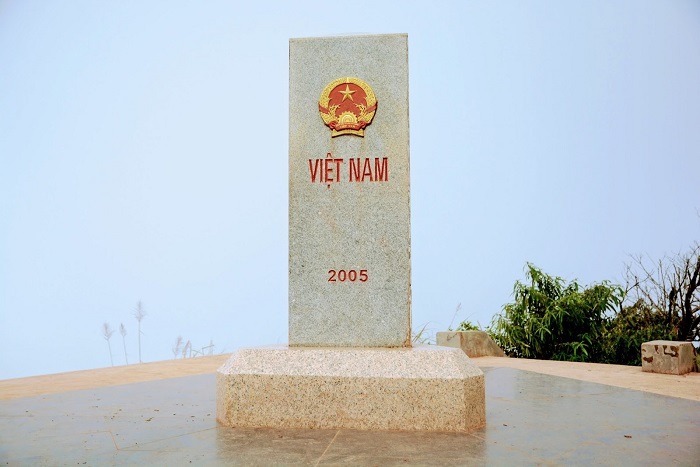 Cột mốc biên giới Việt Nam năm 2005, bầu trời xanh, quốc huy nổi bật, cảnh quan thiên nhiên hùng vĩ.