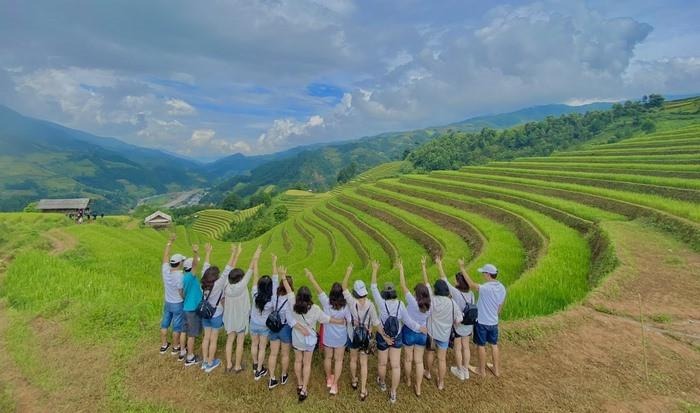 Một nhóm thanh niên đứng trước ruộng bậc thang xanh ngát ở vùng núi phía Bắc Việt Nam, giơ tay chào mừng.