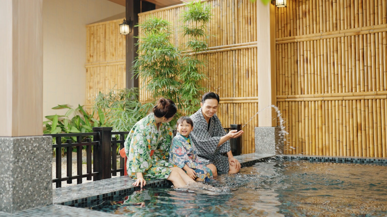 Gia đình mặc yukata thư giãn bên hồ nước, bóng tre xanh trang trí nền.