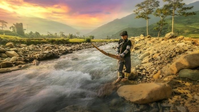 Người đàn ông câu cá trên dòng suối trong cảnh thiên nhiên hùng vĩ dưới ánh chiều tà.