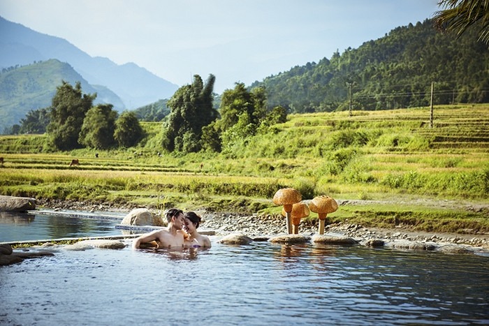 Đôi tình nhân thư giãn trong suối nước nóng giữa cảnh quan thiên nhiên xanh tươi và núi non trùng điệp.