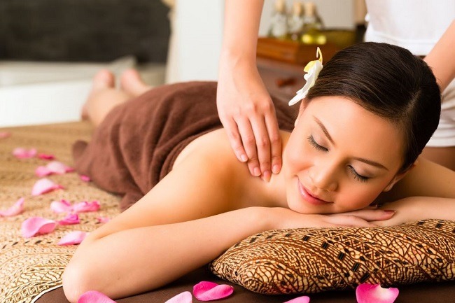 Người phụ nữ thư giãn với liệu pháp massage, nằm trên giường trải hoa hồng, không gian spa thư thái.