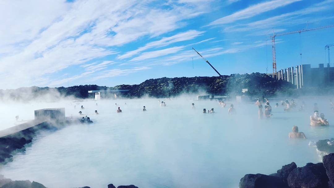 Mọi người thư giãn ở suối nước nóng Blue Lagoon, Iceland, dưới bầu trời trong xanh và làn sương phủ mờ.