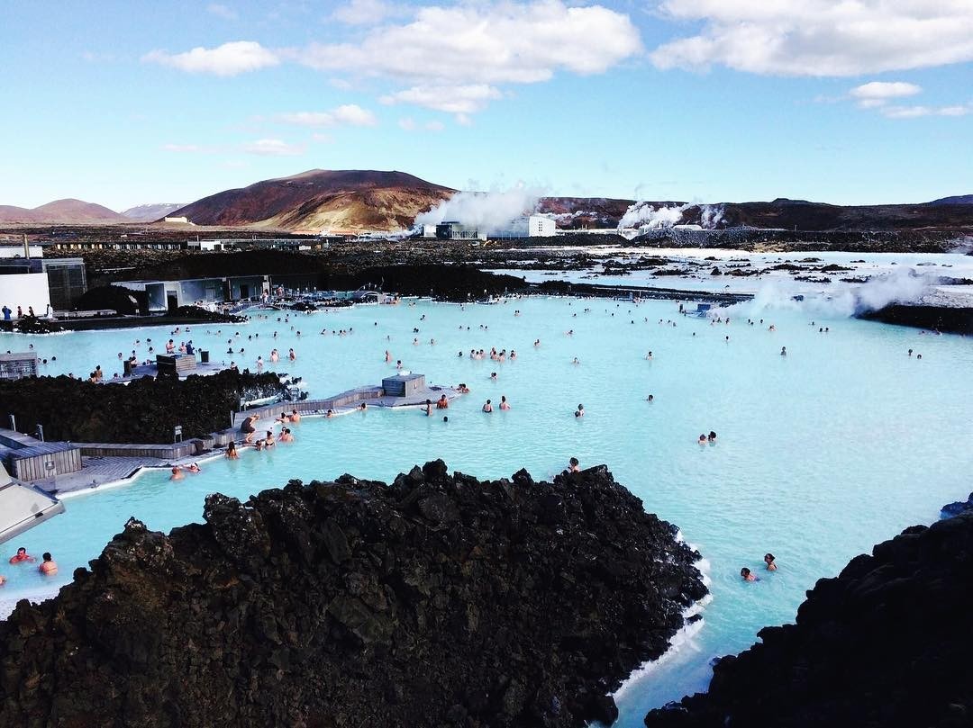 Hồ nước nóng Blue Lagoon, Iceland với nước xanh biếc, núi đá xung quanh và nhiều du khách thư giãn tắm nước nóng.