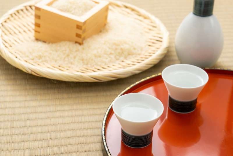 Đĩa sake Nhật Bản, hai ly trắng trên mâm đỏ, rượu và gạo trong nền truyền thống.