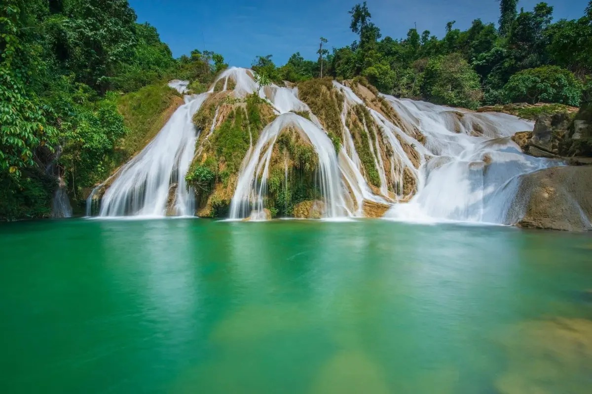 Cảnh thiên nhiên hoang sơ với thác nước tuyệt đẹp giữa rừng xanh, nước trong xanh và hùng vĩ, tạo nên vẻ thanh bình.