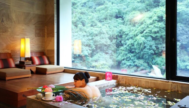 Người phụ nữ thư giãn trong bồn tắm với hoa, view núi, nghỉ dưỡng spa sang trọng.