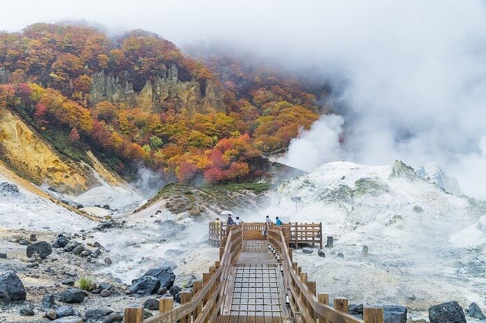 Con đường gỗ dẫn qua thung lũng suối nước nóng trong khung cảnh núi đổi màu vào mùa thu, Hokkaido, Nhật Bản.